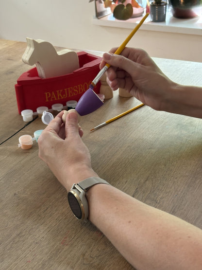 Handen die pietje paars schilderen die hoort bij een DIY knutselset van Sinterklaas.